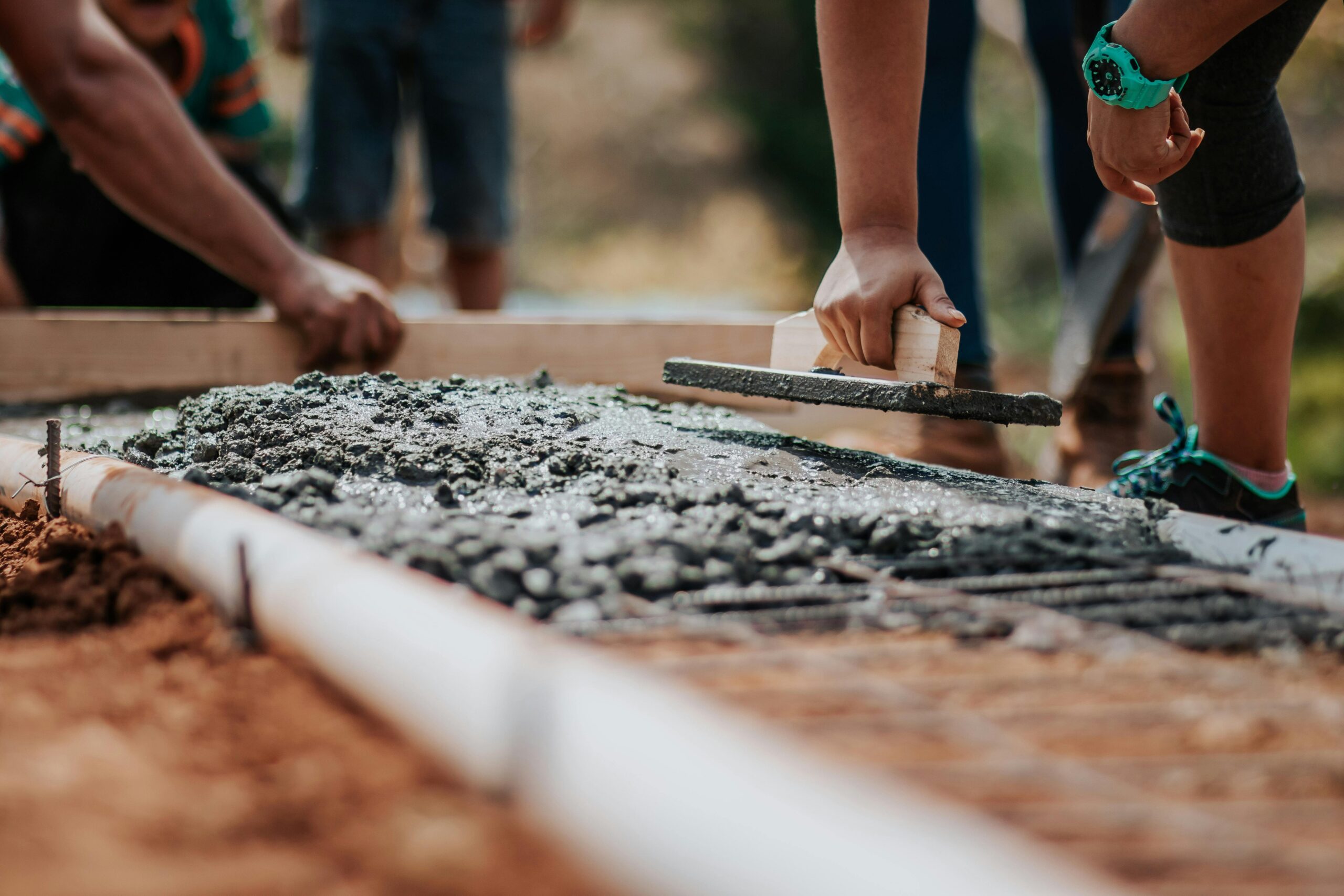 Construction workers leveling fresh cement on a sunny day at an outdoor site.